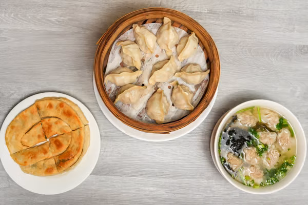 A bamboo steamer of dumplings, a pancake and a bowl of wonton soup