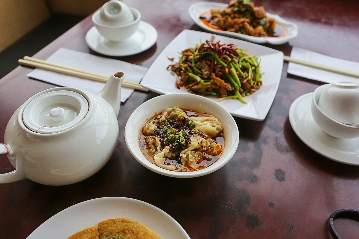 A table set with tea, dumplings in chilli oil and a stir-fried dish